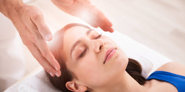 Close-up Of Therapist’s Hand Performing Reiki Treatment On Young Woman In Spa